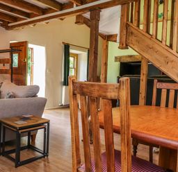A living room with wooden dining chairs a wooden table a gray sofa a small wooden side table and wooden stairs at Bwthyn Gwyn Ty'n Y Pant in Boduan near Nefyn