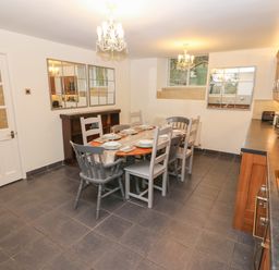 A kitchen dining area with a table set for six chairs and wooden cabinets at Yr Hen Ysgol The Old School in Prenteg