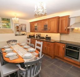 A kitchen with wooden cabinets a dining table set with plates and glasses at Yr Hen Ysgol The Old School in Prenteg
