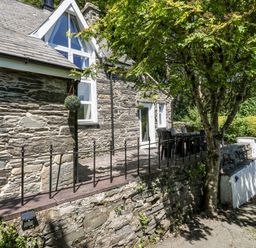 An outdoor patio area with a stone wall and railing outside a stone house with a tree and garden at Yr Hen Ysgol The Old School in Prenteg
