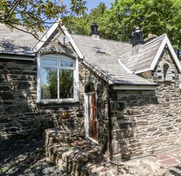 Stone exterior of a cottage with a wooden door and windows surrounded by trees at Yr Hen Ysgol The Old School in Prenteg