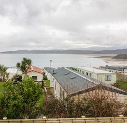 A coastal view with mobile homes trees and a beach at The Sandy Bee in Benllech