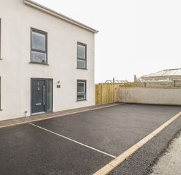 A modern building with a black front door and several windows next to an empty paved parking area at The Sandy Bee in Benllech