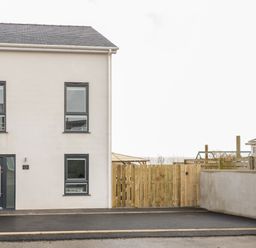 A beige two-story house with dark framed windows and a dark door next to a wooden fence at The Sandy Bee in Benllech