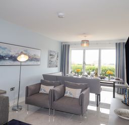 A living room with two armchairs a floor lamp paintings a dining table set and a television at Chandlers Retreat in Newport Pembrokeshire