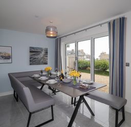 A dining area with a table set for six with yellow flowers next to glass doors at Chandlers Retreat in Newport Pembrokeshire