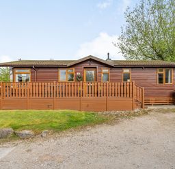 A wooden cabin with a fenced porch and propane tanks outside at Lakeview Lodge in South Lakeland Leisure Village