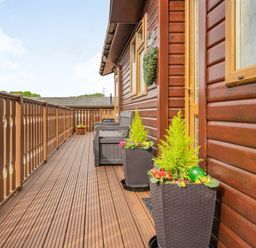 A wooden balcony with railing two planters flowers and a bench at Lakeview Lodge in South Lakeland Leisure Village