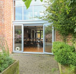 A patio with plants and wooden fence opening to a dining area with wooden table and chairs at The Barn in Tunstead near Hoveton & Wroxham