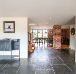 An open room with slate tile floor a black console table on the left and a dining area with black chairs and brick walls at The Barn in Tunstead near Hoveton & Wroxham