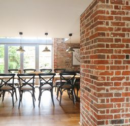 A dining area with a wooden table and black chairs near glass doors and brick walls at The Barn in Tunstead near Hoveton & Wroxham