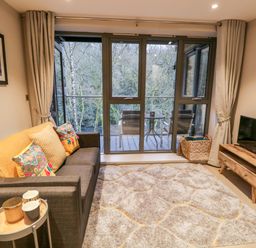 A living room with a gray sofa and patterned cushions next to a coffee table and a wooden TV stand with a television at River View in Backbarrow