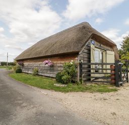 A thatched cottage with wooden siding and flower baskets near a road at The Barn at Rapps Cottage in Rapps near Ilminster