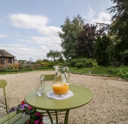 A green table with a jug of orange juice and glasses in a garden at The Barn at Rapps Cottage in Rapps near Ilminster