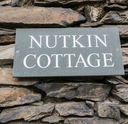 A stone wall with a rectangular sign reading Nutkin Cottage at Nutkin Cottage in Bowness-On-Windermere