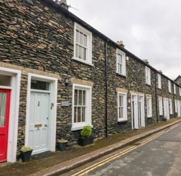 A row of stone cottages with white framed windows and different colored doors along a narrow street at Nutkin Cottage in Bowness-On-Windermere