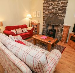 A sitting room with sofas coffee table stone fireplace and television at Nutkin Cottage in Bowness-On-Windermere