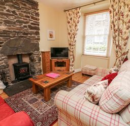 A living room with a stone fireplace a wood stove a wooden coffee table a TV a red sofa and a checked sofa at Nutkin Cottage in Bowness-On-Windermere