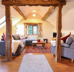 A living room with wooden beams a gray sectional sofa a wooden coffee table and a television at Yr Hen Felin in Llanfyllin