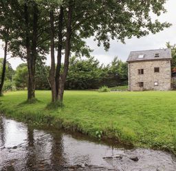 A stone house with a grassy yard and trees next to a stream at Yr Hen Felin in Llanfyllin