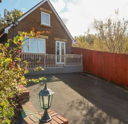 A driveway with a brick house with balcony and a red wooden fence at Ffau'r Ddraig in Cross Hands