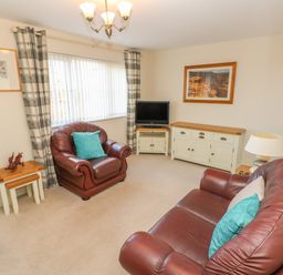 A living room with two brown leather sofas a television on a white stand a wooden sideboard a lamp and framed pictures at Ffau'r Ddraig in Cross Hands