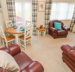 A living room with a round dining table set for four and three brown leather armchairs at Ffau'r Ddraig in Cross Hands