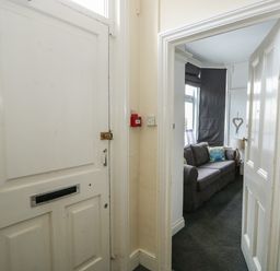A hallway with a white door and an open door leading to a living room with a gray sofa and cushions at Northgate Ground Floor Flat in Hunstanton