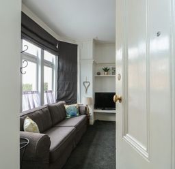 A living room with a dark sofa pillows a lamp a television and window blinds at Northgate Ground Floor Flat in Hunstanton