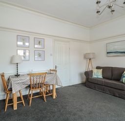 A living room with a sofa and pillows next to a dining table with chairs and lamps at Northgate Ground Floor Flat in Hunstanton