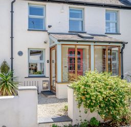 Front view of a two-story house with a small porch and windows with light blue frames at Sea Pickle Cottage in Llangwm Pembrokeshire