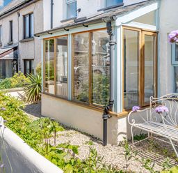 An outdoor garden area with plants a white metal bench and a glass conservatory attached to a row of houses at Sea Pickle Cottage in Llangwm Pembrokeshire