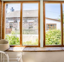 A window with wooden frames looking out to stone and white houses and greenery at Sea Pickle Cottage in Llangwm Pembrokeshire