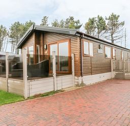 An exterior view of a wooden cabin with glass patio enclosure and a brick driveway at Huckleberry in Runswick Bay near Staithes