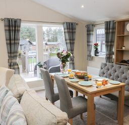 A dining area with a wooden table set with plates and glasses of orange juice next to a sofa and armchair at Huckleberry in Runswick Bay near Staithes