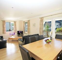 A living room and dining area with black leather sofas a wooden dining table with black chairs and a bowl of fruit at Waters Edge in Falmouth