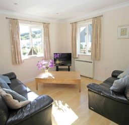 A living room with two black leather sofas a wooden coffee table with flowers and a television at Waters Edge in Falmouth