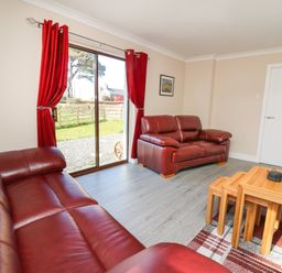 A living room with red leather sofas wooden nesting tables and red curtains at Glyn Cottage in Llanon