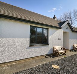 Exterior view of a white cottage with two wooden benches and gravel in front at Glyn Cottage in Llanon