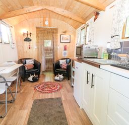 A small kitchen and sitting area with two black chairs a white table with chairs a microwave and sink at Hugatree in Little Dunham near Litcham