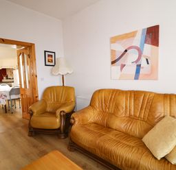 A living room with a leather sofa and armchair next to a lamp and an abstract painting on the wall at Ard an Phiobaire in An Luinnigh near Derrybeg County Donegal