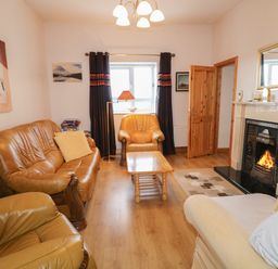 A living room with leather sofas a wooden coffee table a fireplace with a fire a window with curtains and a standing lamp at Ard an Phiobaire in An Luinnigh near Derrybeg County Donegal