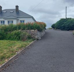 A driveway with hedges and grasses leading to a white house with a dark roof and chimneys at Ard an Phiobaire in An Luinnigh near Derrybeg County Donegal