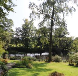 A garden with a bench overlooking a river surrounded by trees at The Old Carriage House in Clappersgate
