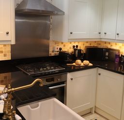 A kitchen with white cabinets black countertops and a brass faucet at The Old Carriage House in Clappersgate