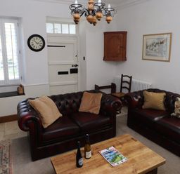 A sitting room with two leather sofas a wooden coffee table clock on the wall and a wooden cabinet at The Old Carriage House in Clappersgate