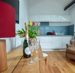 A kitchen area with white cabinets a wooden table with a bottle of champagne and glasses a lamp and tulips and a leather armchair at Old Sawrey Stores in Hawskhead