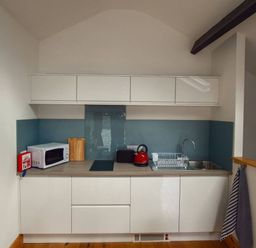 A kitchen area with white cabinets a microwave a red kettle a toaster a sink and a dish rack at Old Sawrey Stores in Hawkshead