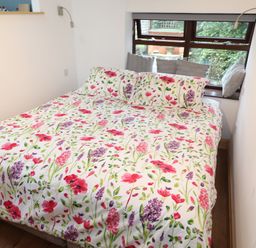 A bedroom with a bed with floral bedding and pillows by a window with cushions at Old Sawrey Stores Hawskhead