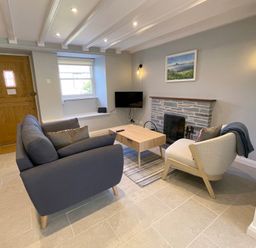 A living room with a gray sofa a beige armchair a wooden coffee table a fireplace and a wall-mounted TV at Kernyk in Perranuthnoe